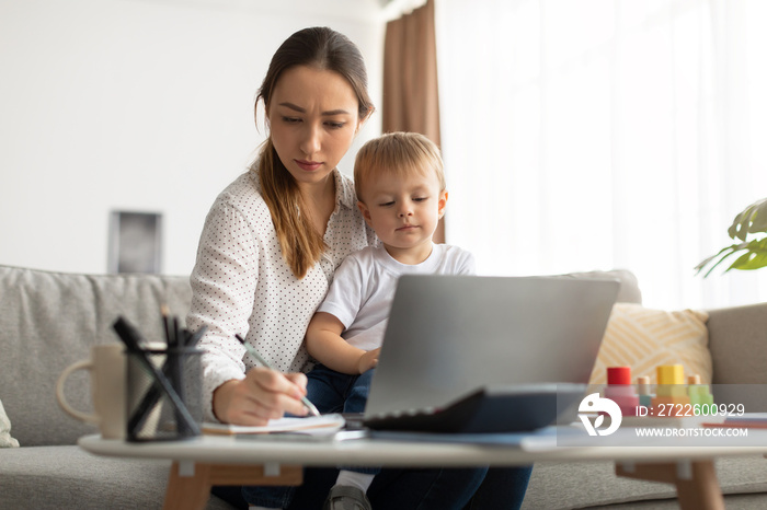 Distance learning. Young lady with child studying online, watching webinar and writing notes in notepad