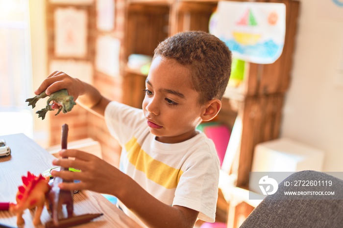 Beautiful african american toddler playing with dinosaurs toy on desk at kindergarten