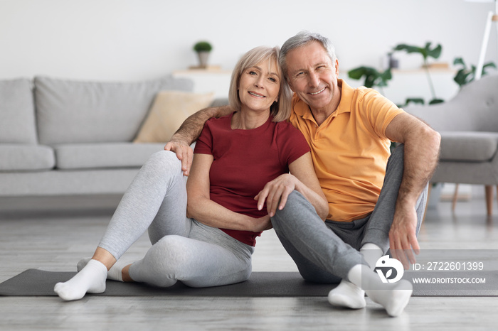 Happy elderly couple sitting on fitness mat at home