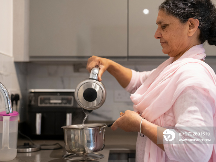 Mature woman in traditional clothing pouring water for tea in kitchen