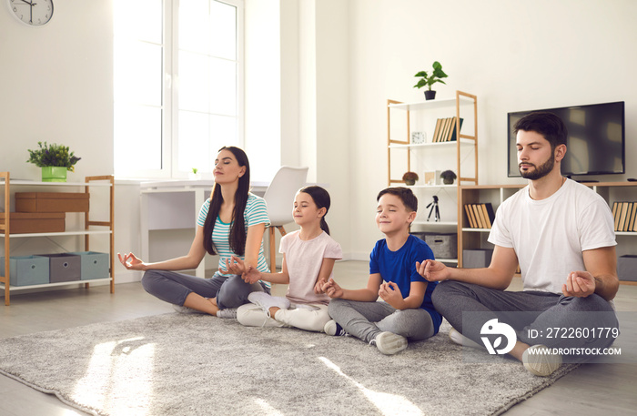 Healthy mind in healthy body. Millennial family with little children doing yoga at home. Happy young couple with calm kids sitting legs crossed on warm floor rug and practicing meditation together