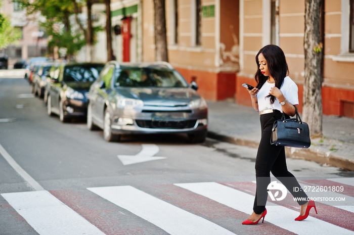 Stylish african american business woman on streets of city at pedestrian crossing.