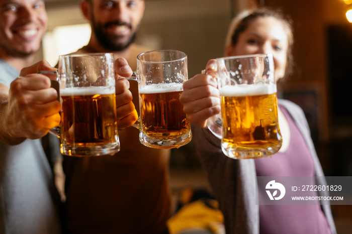 Group of happy friends drinking and toasting beer at bar