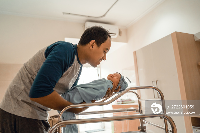 Young smiling father putting his newborn baby in crib in the hospital