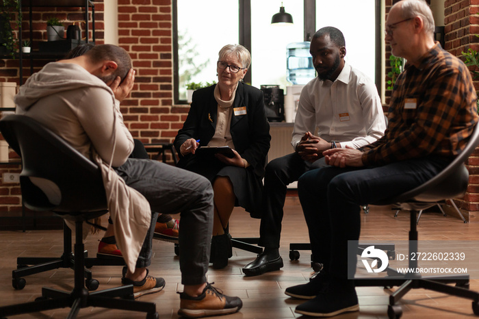 AA meeting group comforting man with depression issues at therapy session. Patients attending rehabilitation program and trying to cure alcohol addiction and anxiety. Concept of rehab