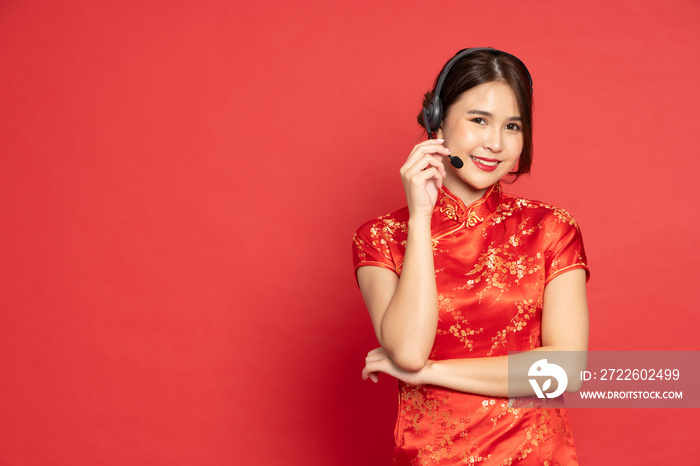 Asian call center or customer service wearing red traditional cheongsam qipao with headset isolated on red background, Telemarketing, customer support agent provide service on telephone concept