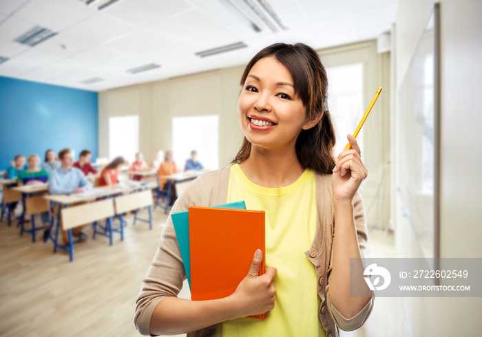 education, high school and knowledge concept - asian female teacher with books and pencil over classroom background