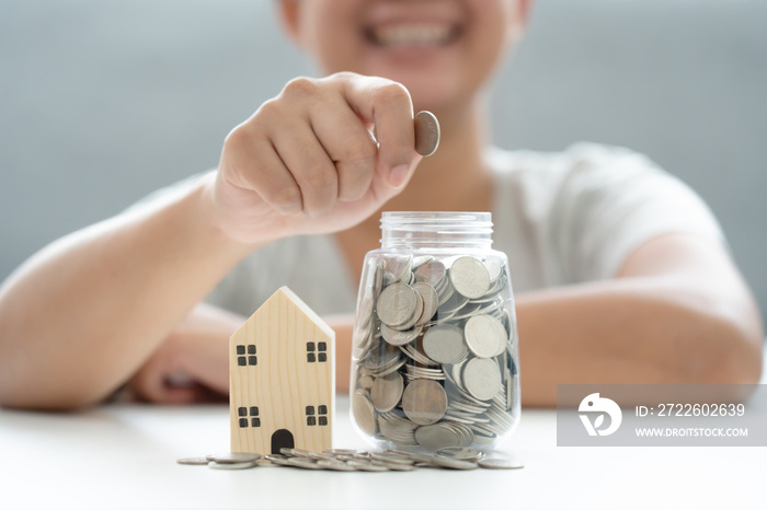 Woman save money coin in jar for new property living investment, wooden house and jar coins savings concept.