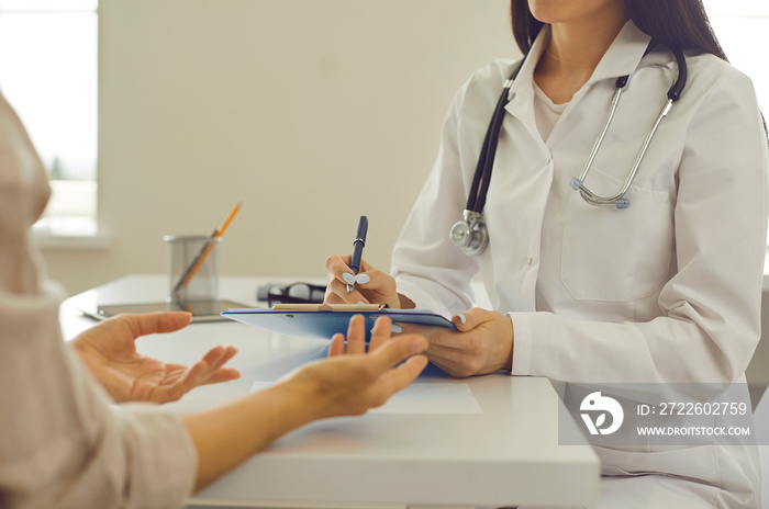 Female therapeutist with clipboard listening to patient and noting down her health complaints