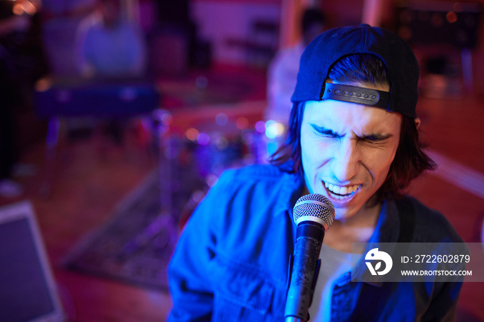 Portrait of music artist singing passionately to microphone in live performance, copy space