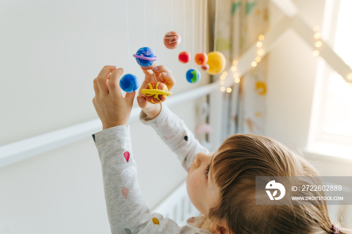 Little girl playing with toy planets made by herself from colorful molding clay indoor