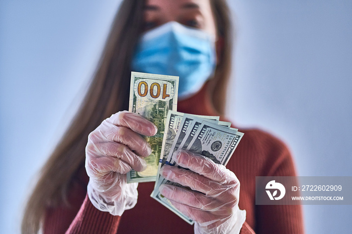 Woman in medical protective mask and transparent protective gloves counts money. Health and hand protection during flu covid outbreak and coronavirus epidemic. Virus money concept