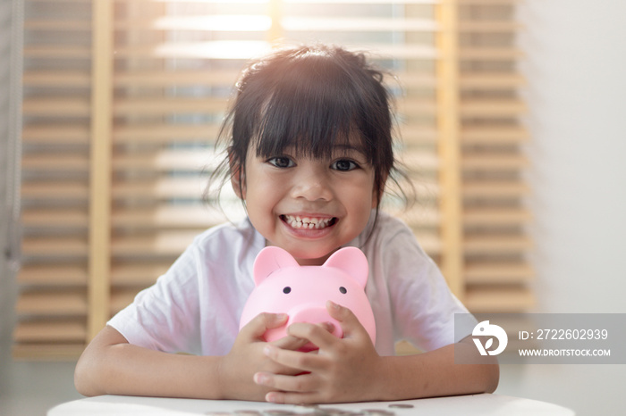 Little Asian girl saving money in a piggy bank, learning about saving, Kid save money for future education. Money, finances, insurance, and people concept