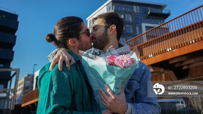 Smiling gay couple with bouquet kissing outdoors