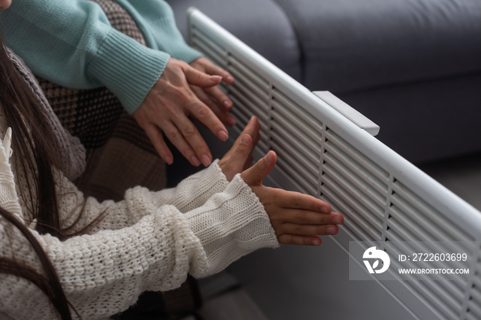 Family warming hands near electric heater at home, closeup