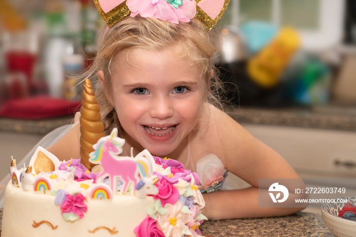 Little girl smiles next to her unicorn birthday cake
