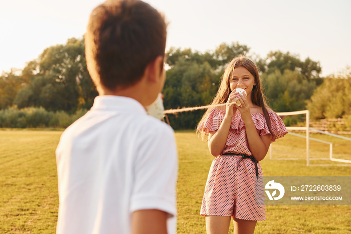 Boy with girl having fun by using tin can telephone while standing outdoors on the field