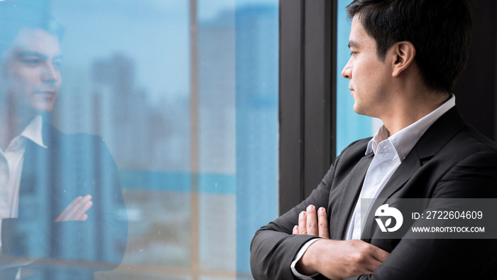 Confident young business man in the office looking out of the window.