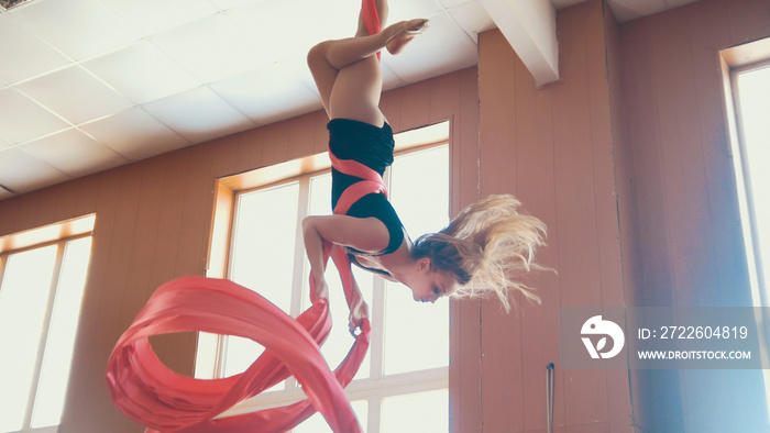 Attractive girl air gymnast hangs upside down and waving the aerial silk