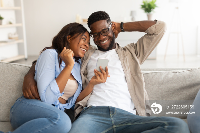 African american couple sitting on couch, using cellphone