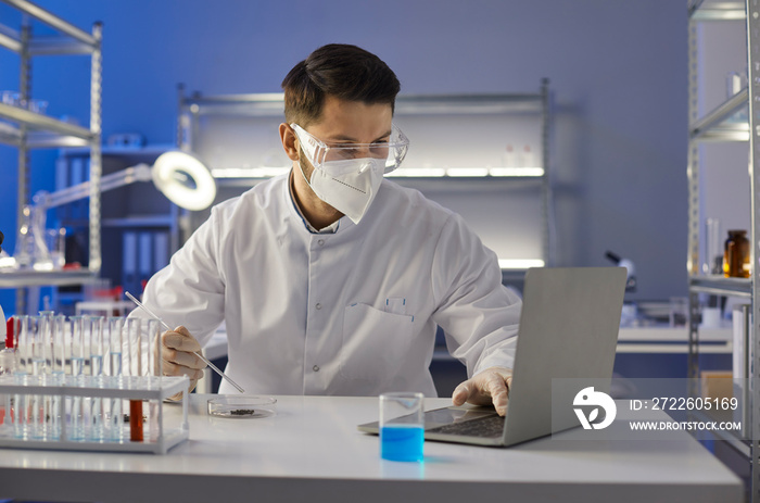 Scientist in glasses and mask doing research in science laboratory. Lab worker, assistant or medical university student in goggles entering data analysis report in electronic system on laptop computer