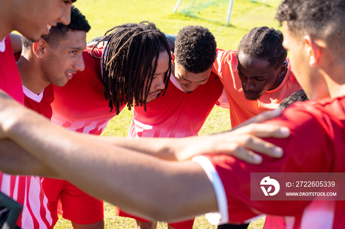 Multiracial male soccer players with arms around huddling and discussing in playground during match