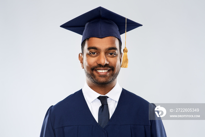 education, graduation and people concept - happy smiling indian male graduate student in mortar board and bachelor gown over grey background