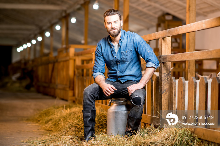 Portrait of a handsome farmer sitting on the retro milk container at the goat barn. Natural milk production and farming concept