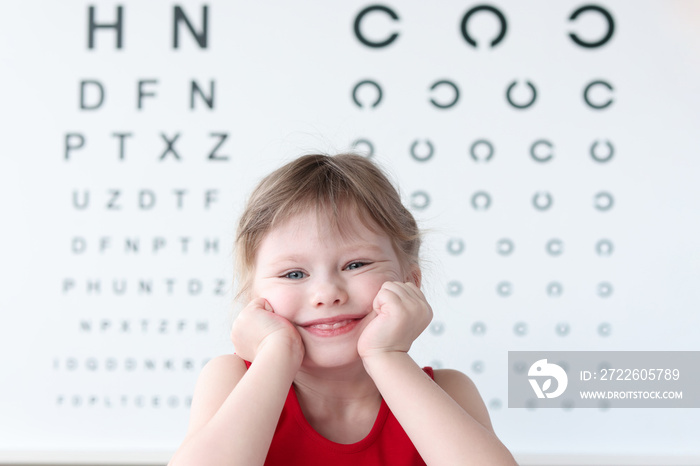 Smiling little child against vision test table in medical clinic portrait. Health and happy childhood concept