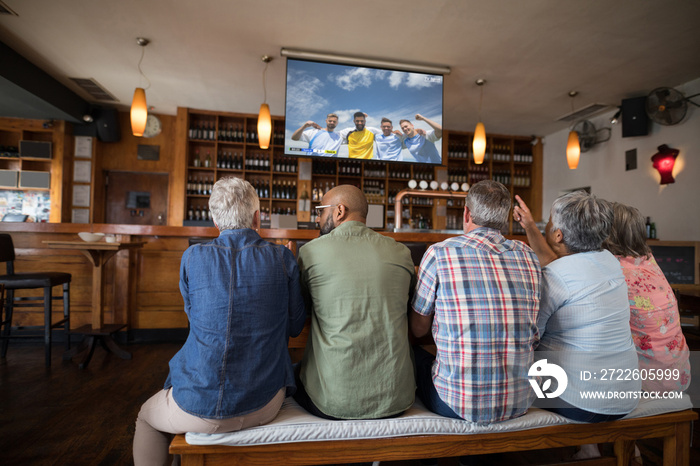 Group of senior diverse friends sitting in the bar and watching football match