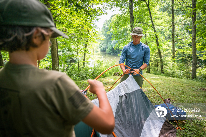 Air Force service member sets up a tent with his sons on  a backpacking trip.