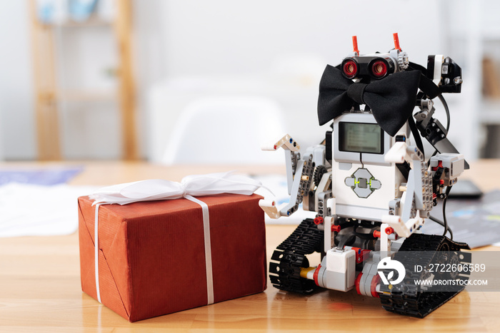 Romantic smart robot standing next to gift box indoors