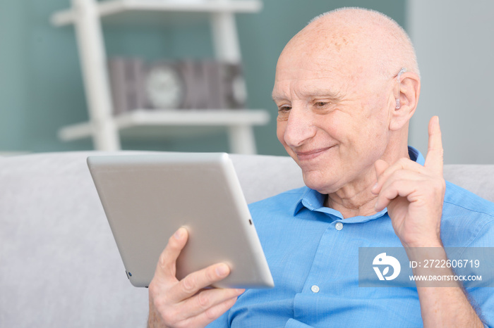 Senior man with hearing aid using tablet computer indoors