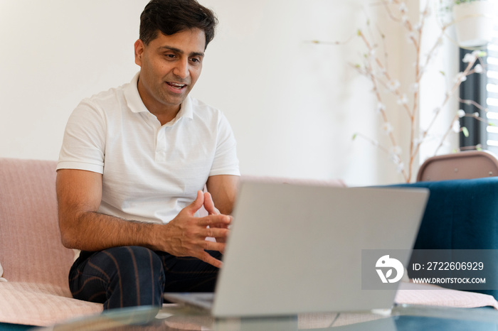 Man talking using laptop while sitting on sofa at living room