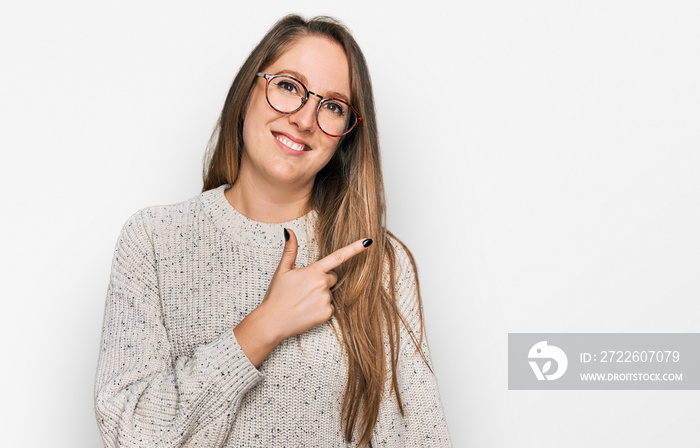 Young blonde woman wearing casual sweater and glasses cheerful with a smile of face pointing with hand and finger up to the side with happy and natural expression on face