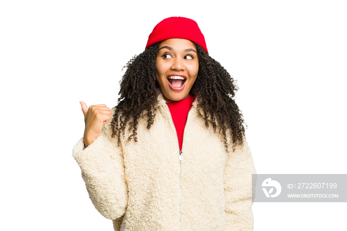 Young african american woman wearing winter clothes isolated points with thumb finger away, laughing and carefree.