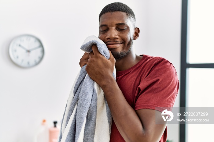 Young african american man smiling confident smelling clean clothes at laundry room