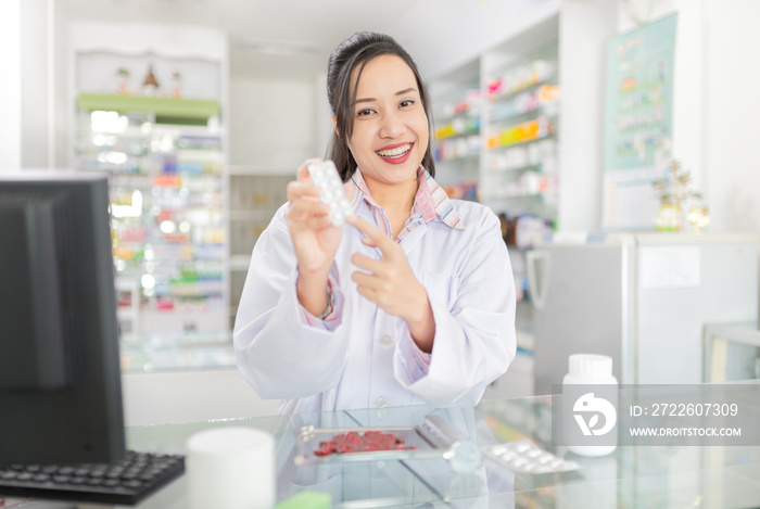 asian female pharmacist explain about how to use drug, she holding drug strip pack with her hand and talk with customer in drugstore