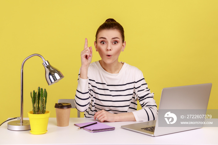 Excited woman manager in striped shirt looking surprised by genius idea, raising finger up inspired by creative thought at workplace. Indoor studio studio shot isolated on yellow background.