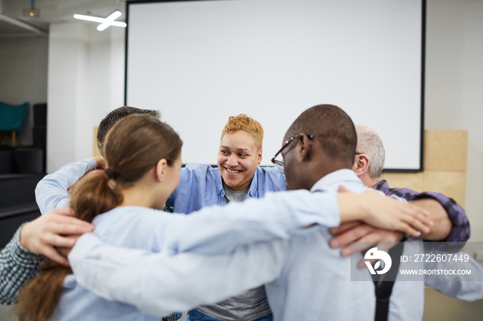 Group of people hugging all together during therapy session in support meeting, copy space