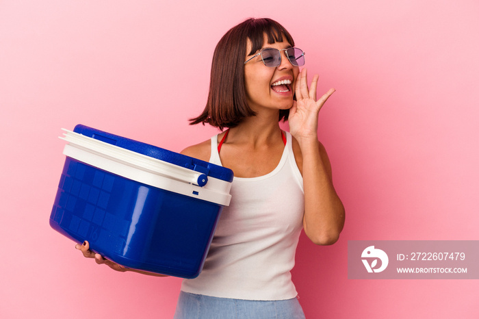 Young mixed race woman holding a cooler isolated on pink background shouting and holding palm near opened mouth.