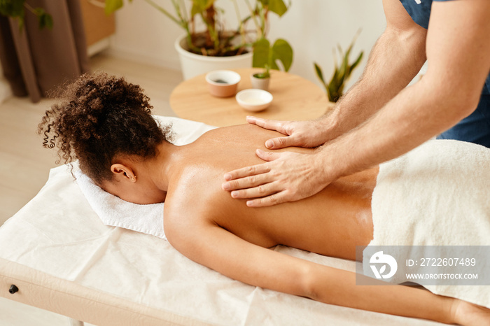 Top view of black young woman lying on spa bed enjoying back massage, copy space