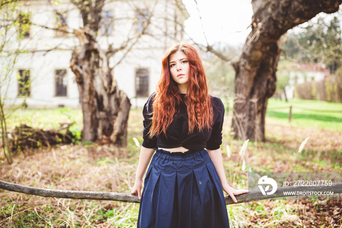 Beautiful redhead young woman looking gloomy at the camera. Outdoor portrait.