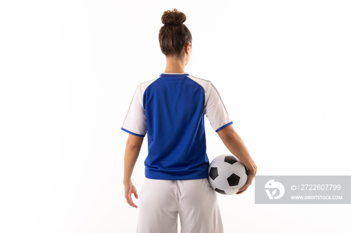Rear view of biracial young female soccer player with soccer ball standing against white background