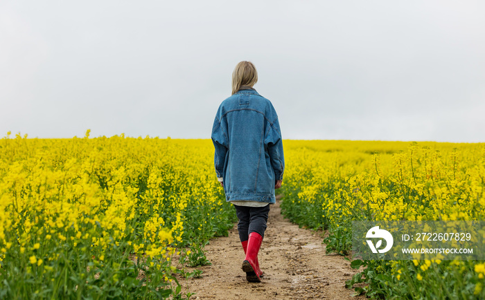 Beautiful blonde in denim jacket and wellington boot on yellow rapeseed field