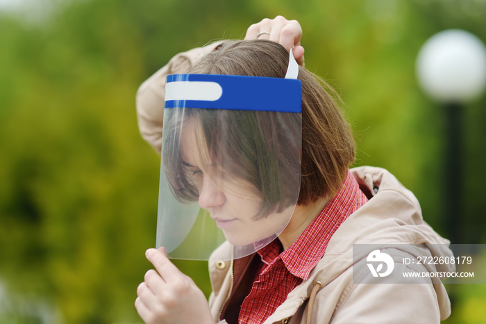 Young woman putting on face shield on street of city or park. Safety during COVID-19 outbreak. Lifting virus lockdown. Social distancing and face mask - security measures when exiting quarantine