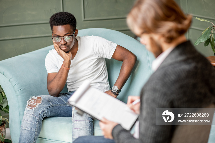 Young afro ethnicity man having a serious conversation with psychologist sitting on the comfortable couch during psychological session in the office