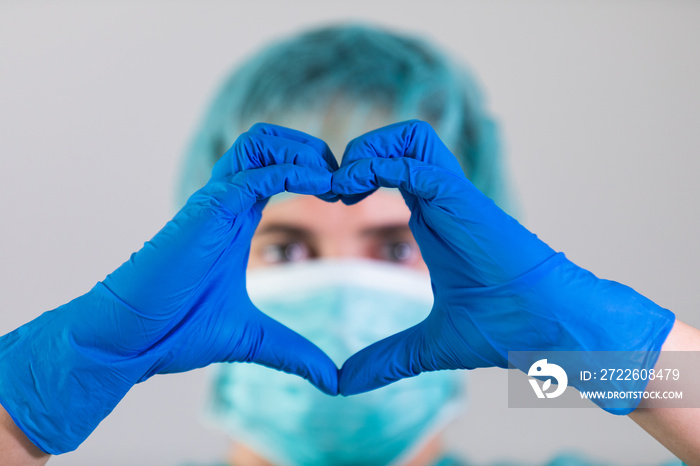 Young woman doctor wearing protective mask against coronavirus. Doctor hands in gloves making shape of heart. Medical personal protection equipment.