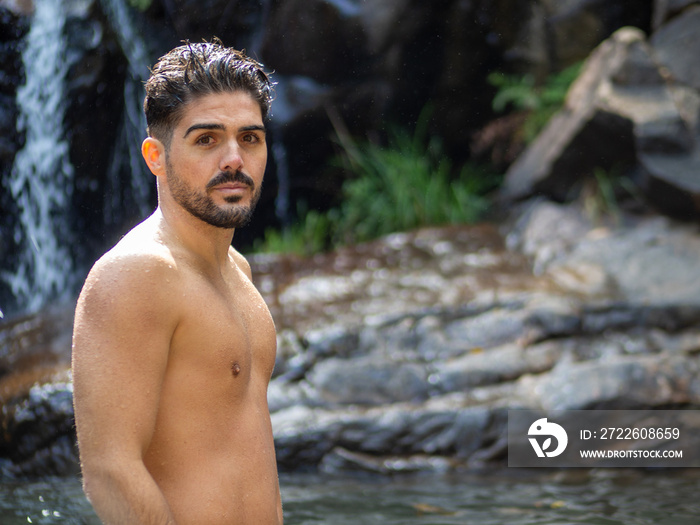 Hombre joven disfrutando de sus vacaciones de verano bañándose en un lago con rocas y una catarata en el fondo. Situado en Bali, Indonesia