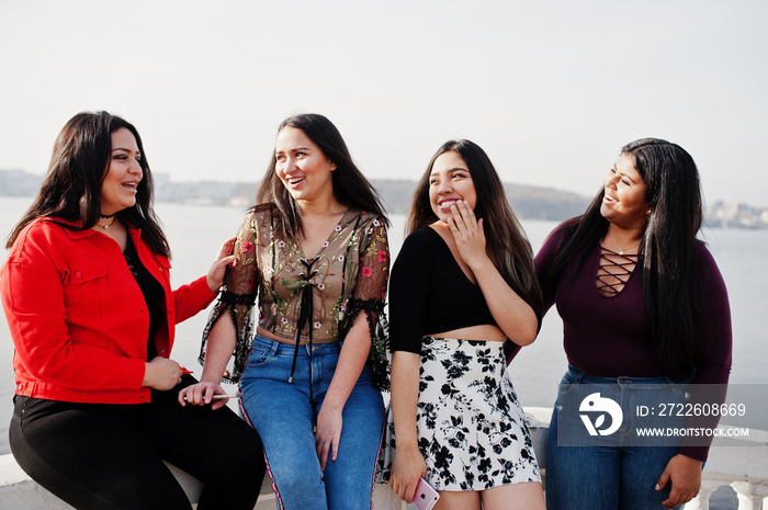 Group of four happy and pretty latino girls from Ecuador posed against lake side.